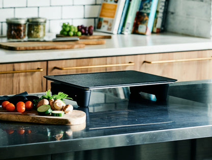 Plită neagră pe blatul bucătăriei, cu legume și cărți în fundal